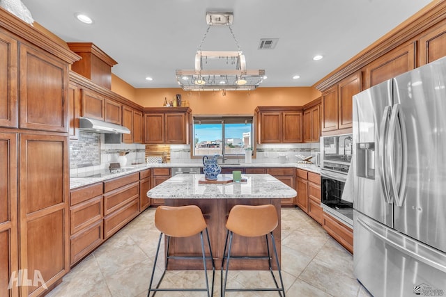 kitchen featuring a breakfast bar, light stone counters, appliances with stainless steel finishes, a kitchen island, and decorative backsplash