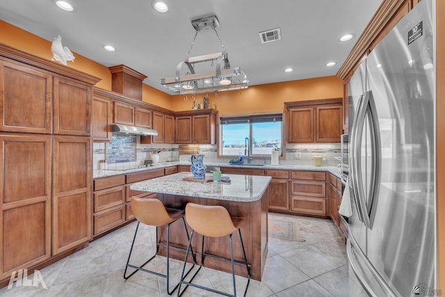 kitchen featuring a kitchen island, stainless steel refrigerator, sink, a kitchen bar, and light stone counters