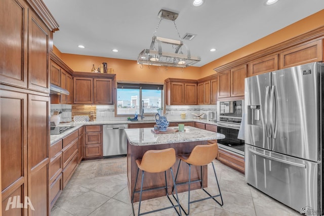 kitchen featuring a breakfast bar area, backsplash, a center island, stainless steel appliances, and light stone countertops