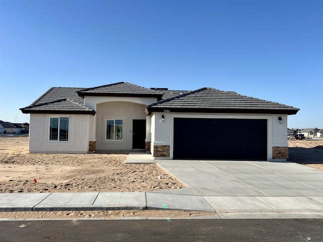 prairie-style house with stone siding, stucco siding, an attached garage, and concrete driveway