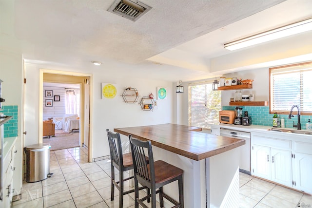 kitchen with a breakfast bar, sink, light tile patterned floors, dishwasher, and white cabinetry