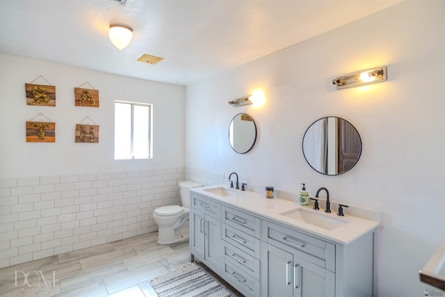 bathroom with vanity, toilet, and tile walls