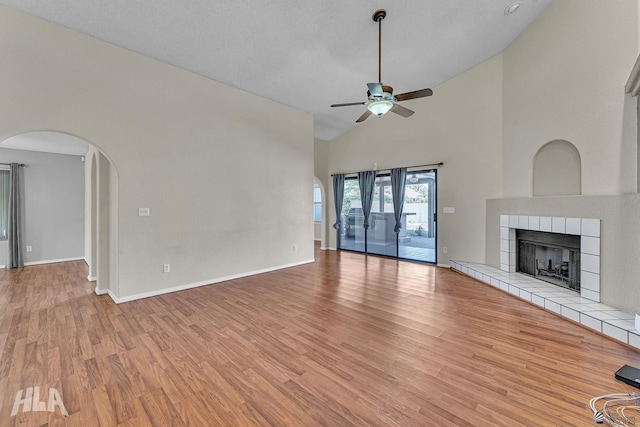 unfurnished living room with arched walkways, high vaulted ceiling, a fireplace, a ceiling fan, and light wood-type flooring