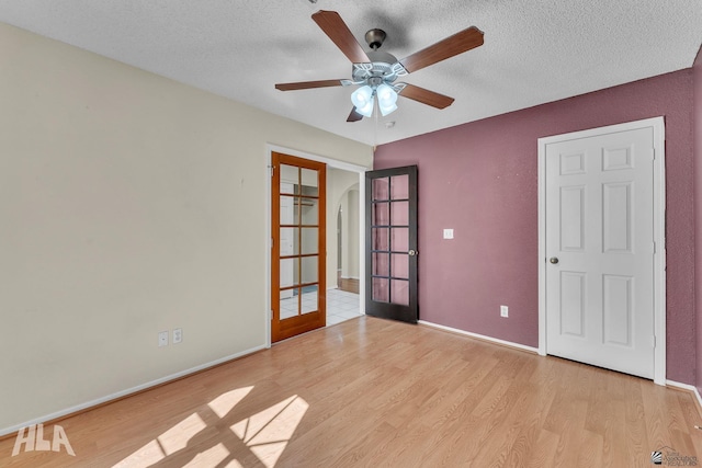 spare room featuring arched walkways, french doors, a textured ceiling, and light wood-style floors