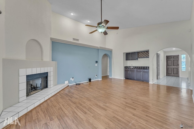 unfurnished living room featuring light wood finished floors, visible vents, arched walkways, and a tile fireplace