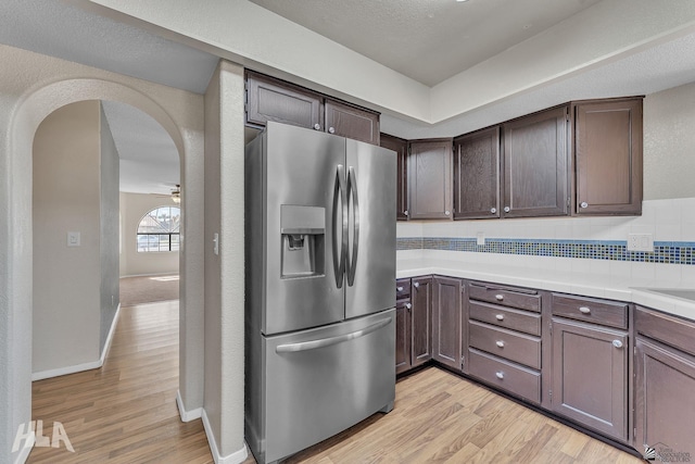 kitchen with arched walkways, stainless steel refrigerator with ice dispenser, light countertops, light wood-style flooring, and dark brown cabinetry