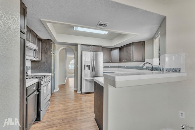 kitchen with arched walkways, stainless steel appliances, a raised ceiling, light countertops, and a peninsula