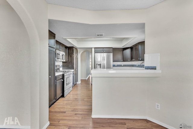 kitchen featuring arched walkways, stainless steel appliances, light countertops, visible vents, and dark brown cabinets