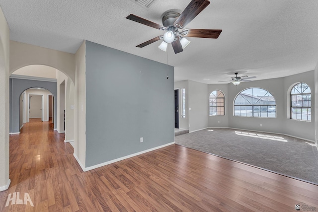 spare room with arched walkways, a textured ceiling, light wood-type flooring, and a wealth of natural light