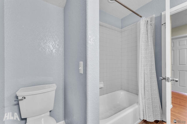 bathroom with toilet, a textured wall, shower / tub combo with curtain, and wood finished floors