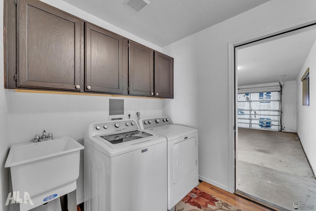 laundry room featuring cabinet space, visible vents, washer and dryer, light wood-type flooring, and a sink