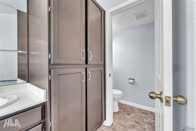 bathroom featuring toilet, vanity, visible vents, and baseboards