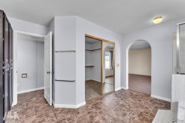 interior space with arched walkways, a textured ceiling, and baseboards