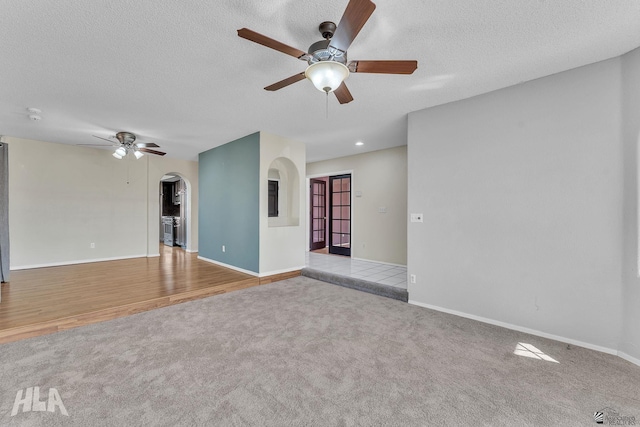 spare room featuring arched walkways, a ceiling fan, light carpet, a textured ceiling, and baseboards