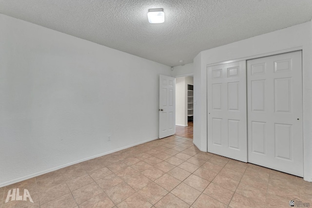 unfurnished bedroom with a closet, light tile patterned flooring, a textured ceiling, and baseboards