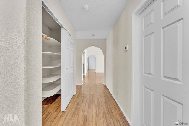 corridor featuring light wood-style floors, baseboards, arched walkways, and a textured ceiling