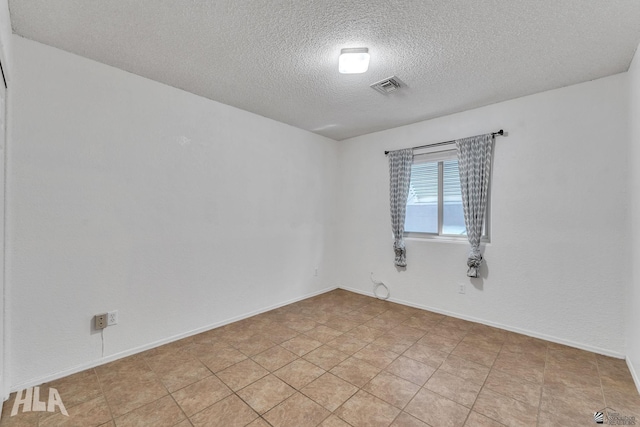 empty room with visible vents, a textured ceiling, and baseboards