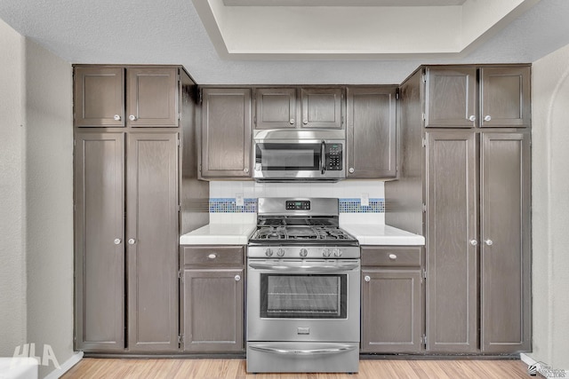 kitchen featuring light wood-type flooring, appliances with stainless steel finishes, light countertops, and decorative backsplash