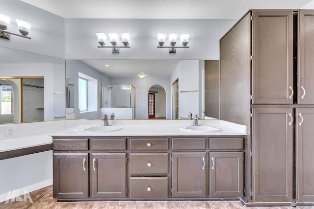 bathroom with a textured ceiling, double vanity, a sink, and a shower stall