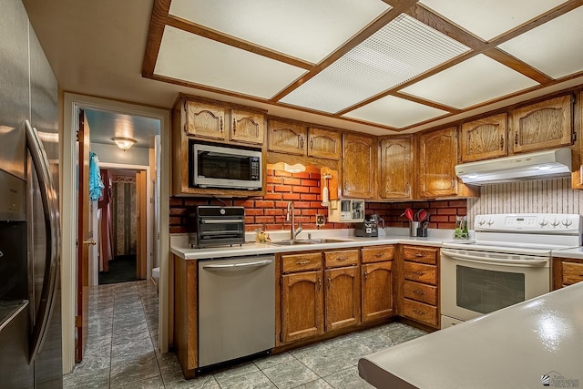 kitchen with light countertops, appliances with stainless steel finishes, brown cabinetry, and under cabinet range hood