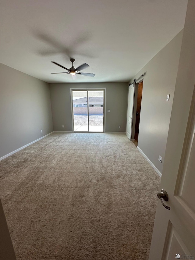 carpeted spare room featuring a barn door and ceiling fan