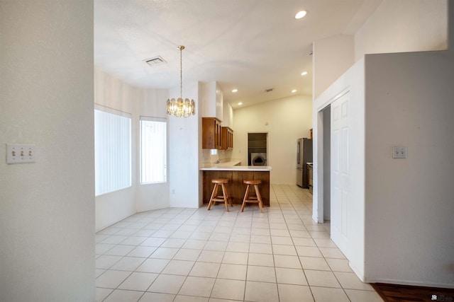 kitchen with an inviting chandelier, vaulted ceiling, light tile patterned floors, stainless steel refrigerator, and kitchen peninsula