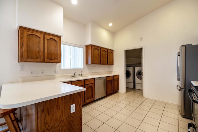 kitchen with light tile patterned flooring, sink, appliances with stainless steel finishes, kitchen peninsula, and washer and clothes dryer