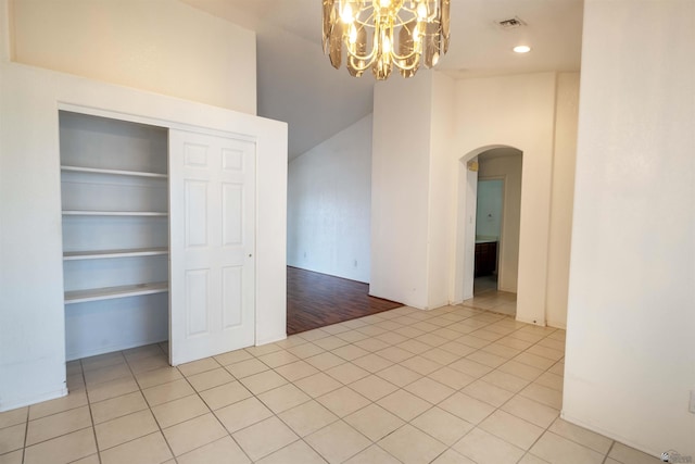 tiled spare room with lofted ceiling, a notable chandelier, and built in shelves