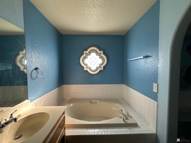 bathroom featuring tiled bath, vanity, and a textured ceiling