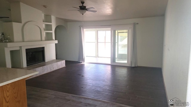 unfurnished living room with ceiling fan, dark hardwood / wood-style flooring, a tile fireplace, and built in shelves