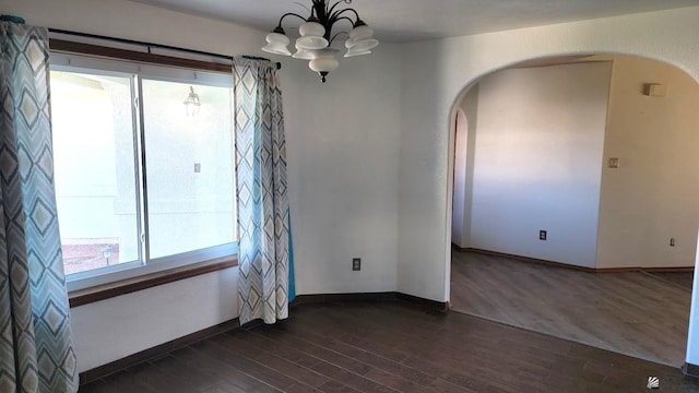 empty room featuring a healthy amount of sunlight, dark hardwood / wood-style floors, and a notable chandelier