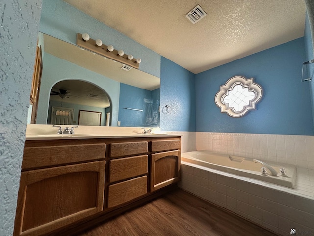 bathroom featuring a textured ceiling, vanity, ceiling fan, tiled bath, and hardwood / wood-style flooring