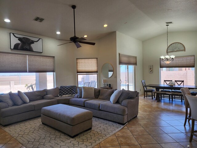 tiled living room featuring ceiling fan with notable chandelier and high vaulted ceiling