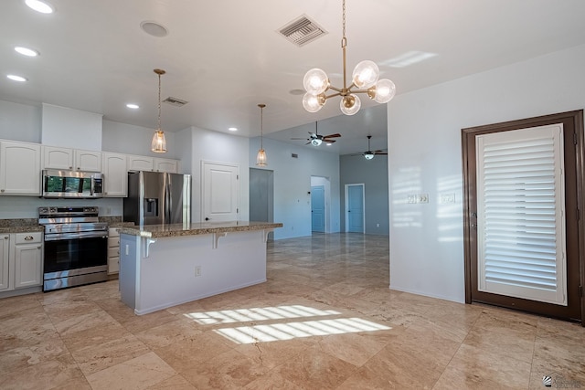 kitchen with light stone counters, stainless steel appliances, decorative light fixtures, a center island, and white cabinetry