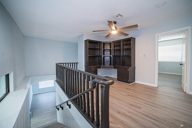 stairway with a textured ceiling, wood finished floors, a ceiling fan, visible vents, and baseboards