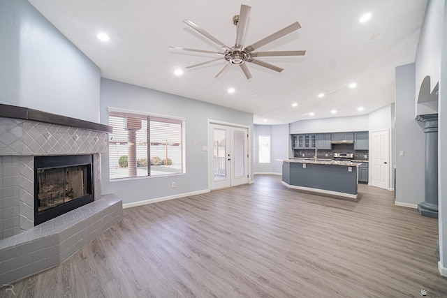 unfurnished living room featuring baseboards, a fireplace with raised hearth, a ceiling fan, lofted ceiling, and light wood-style floors