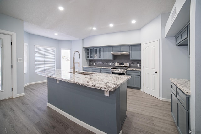 kitchen with stainless steel gas stove, a center island with sink, a sink, gray cabinetry, and backsplash