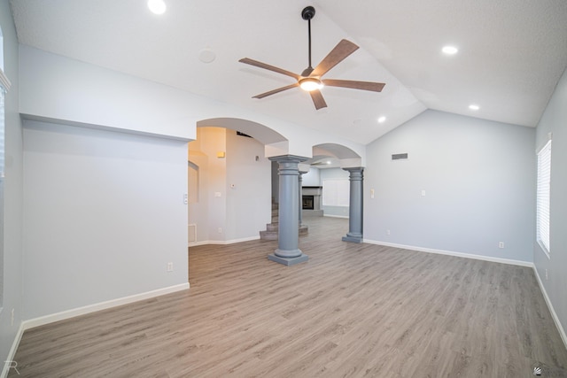 unfurnished living room featuring arched walkways, ceiling fan, lofted ceiling, light wood-style flooring, and ornate columns