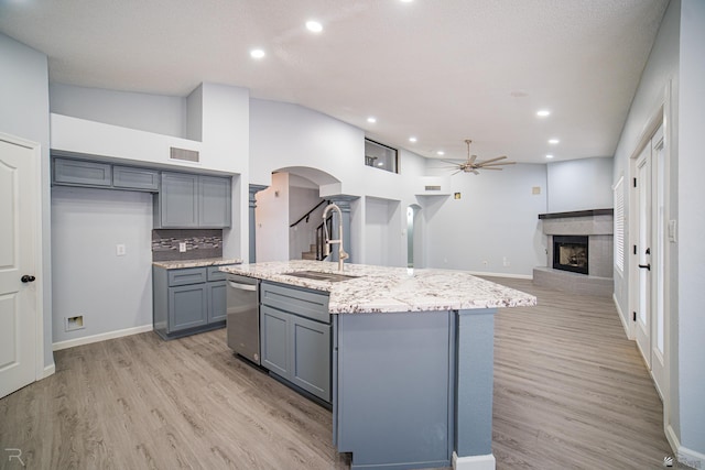 kitchen featuring arched walkways, gray cabinetry, a sink, a brick fireplace, and light wood finished floors