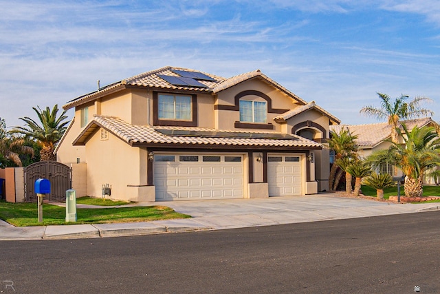 mediterranean / spanish-style house with a garage, concrete driveway, a gate, roof mounted solar panels, and stucco siding