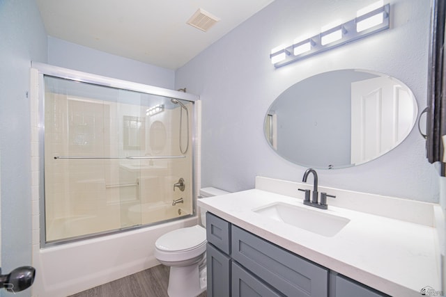 bathroom featuring visible vents, toilet, enclosed tub / shower combo, vanity, and wood finished floors