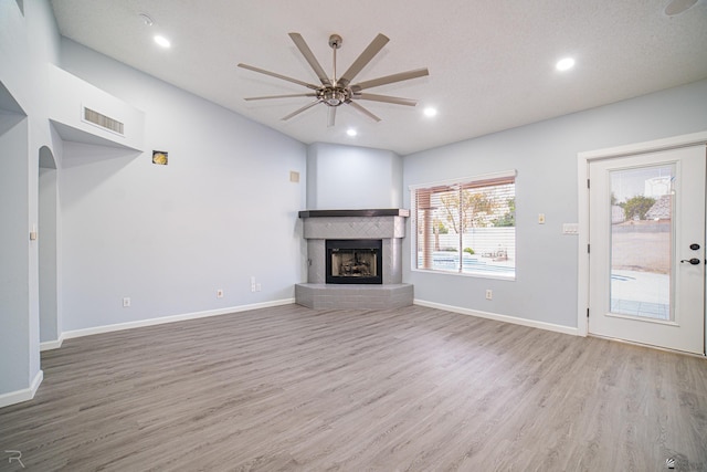 unfurnished living room featuring a fireplace with raised hearth, ceiling fan, wood finished floors, and visible vents