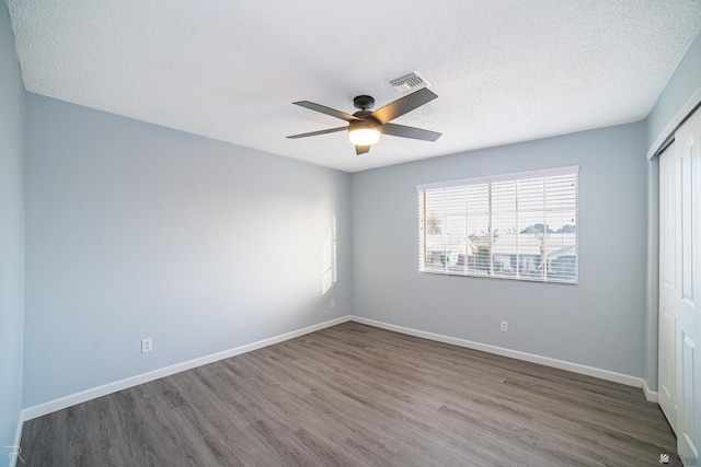 empty room featuring visible vents, a textured ceiling, baseboards, and wood finished floors