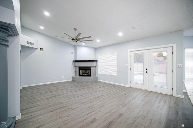 unfurnished living room featuring baseboards, a fireplace with raised hearth, wood finished floors, french doors, and recessed lighting