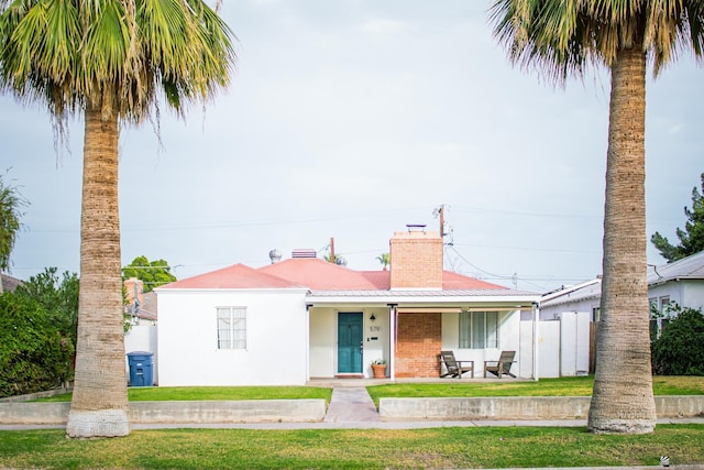 view of front of house with brick siding, a chimney, stucco siding, metal roof, and a front lawn