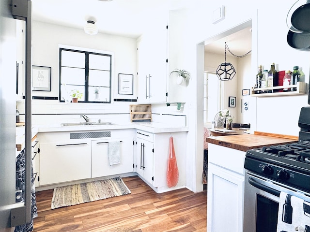 kitchen featuring light wood finished floors, backsplash, white cabinets, stainless steel range with gas stovetop, and a sink