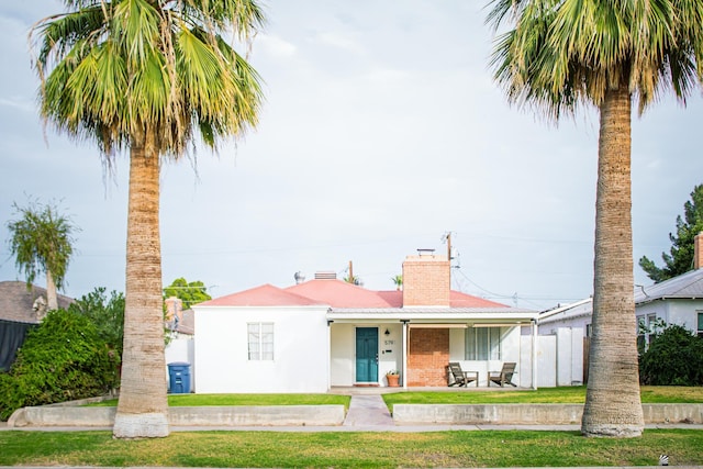 view of front facade featuring a porch, brick siding, stucco siding, a chimney, and a front yard