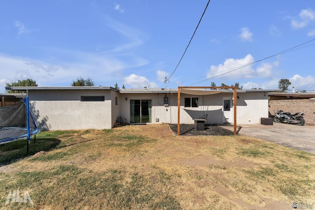 rear view of property featuring a trampoline, a patio area, and a lawn