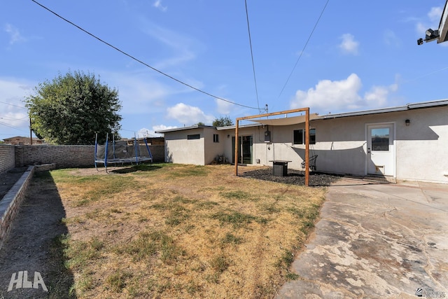 rear view of property featuring a trampoline, a yard, stucco siding, a patio area, and a fenced backyard