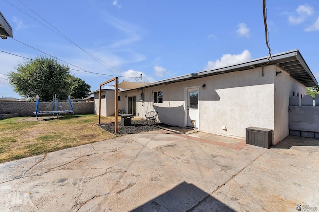 rear view of property with a trampoline, a yard, a patio, stucco siding, and fence